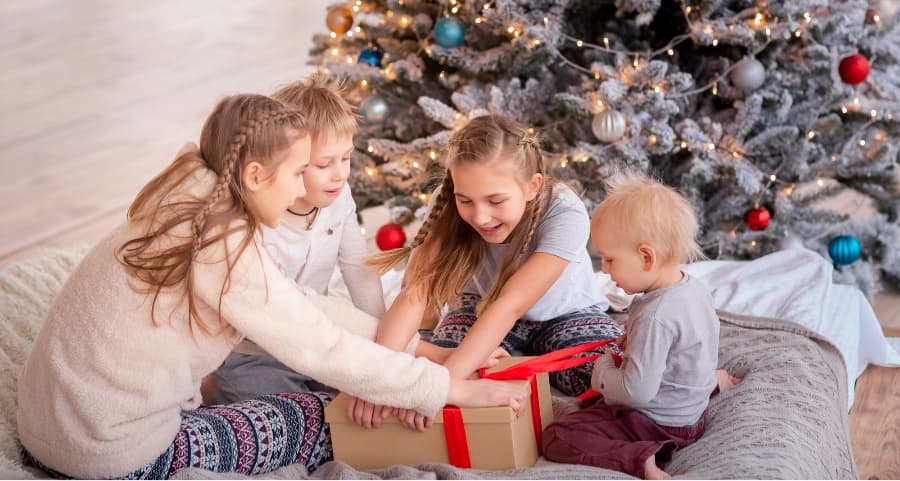 Children opening a present next to a Christmas tree.